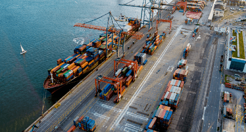 a busy port area with cranes, ships, and shipping containers preparing for transport