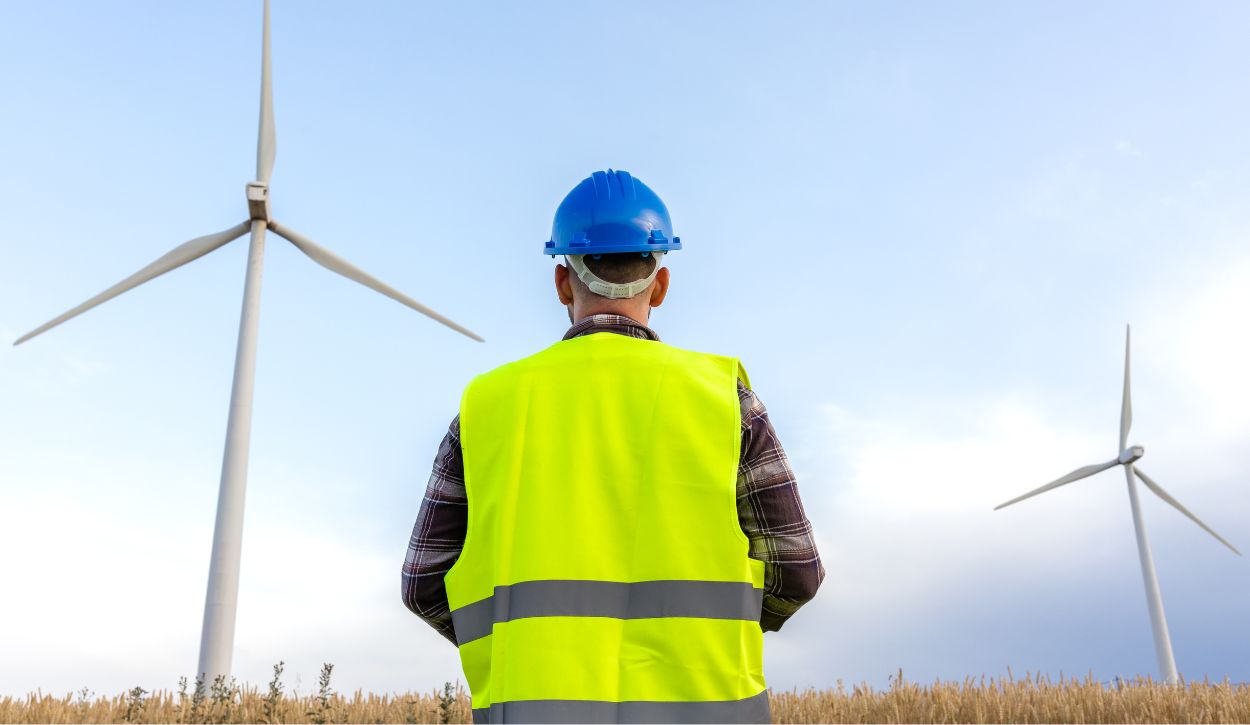 Picture of worker in yellow vest standing in front of wind turbines
