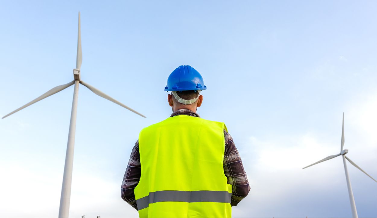Maintenance worker standing behind two large horizontal-axis wind turbines