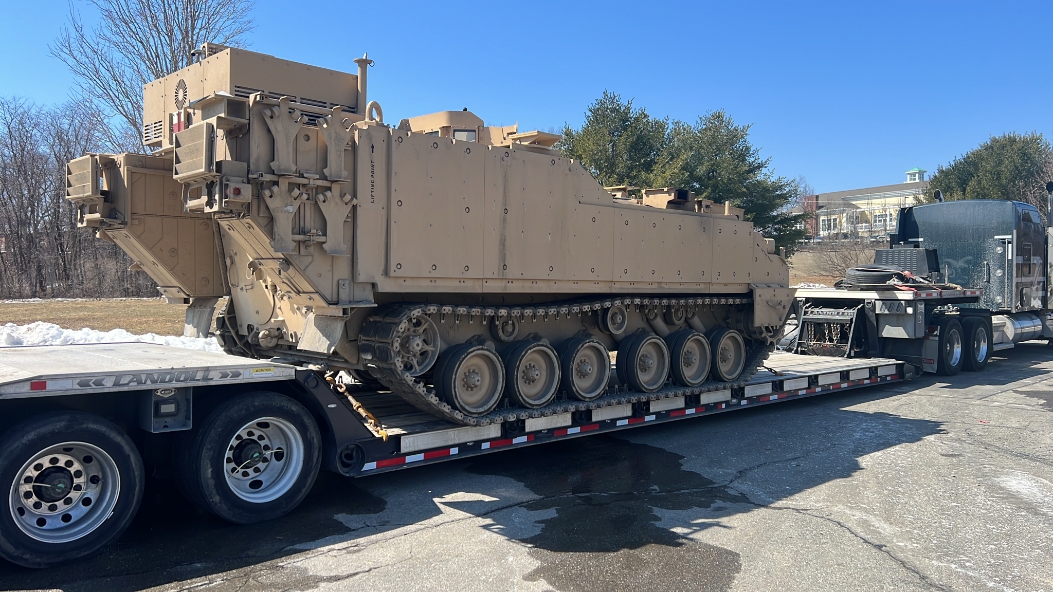 An oversized Army tank being transported from a secure defense facility in Devens, Massachusetts to an event center in Huntsville, Alabama. The tracked military vehicle is secured on a multi-axle removable gooseneck (RGN) lowboy trailer, highlighting Titan Worldwide’s expertise in handling heavy, wide, and overweight defense logistics.
