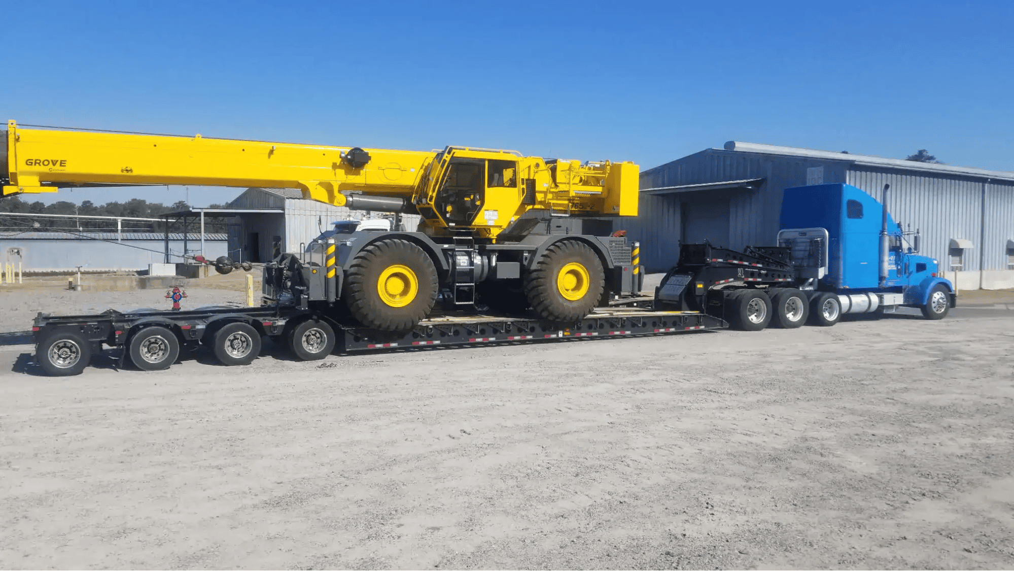 Blue semi-truck hauling yellow crane on lowboy trailer