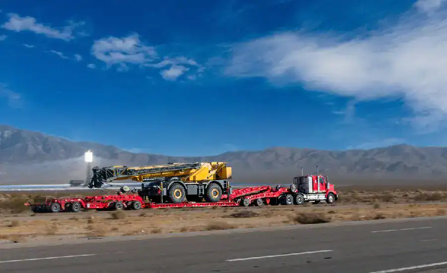Red semi truck hauling yellow crane through desert.