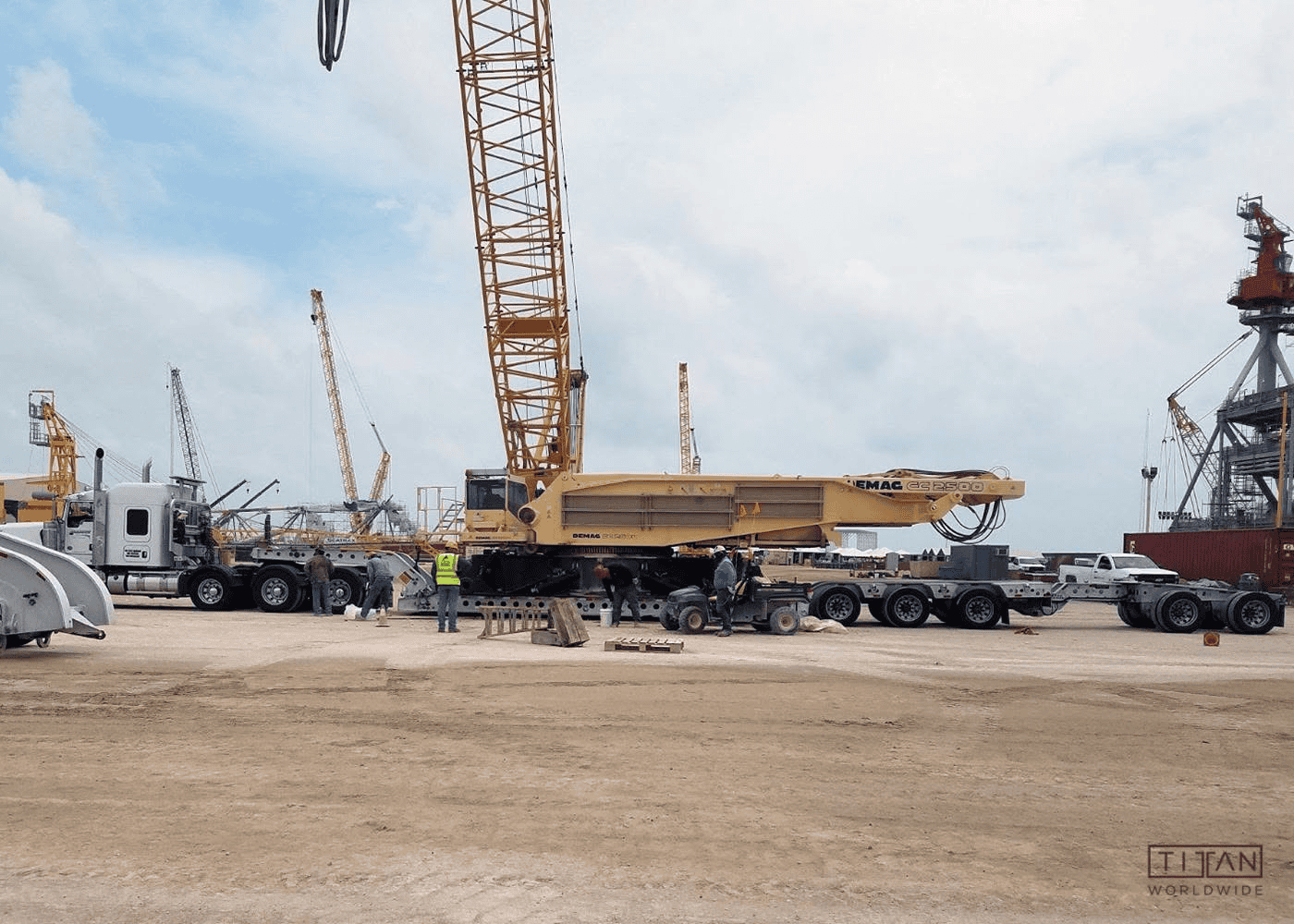 Crane assembly at port with workers and trucks.